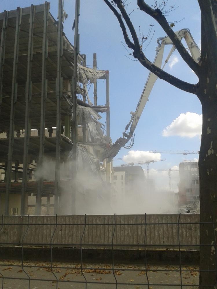 Ein großer Abrissbagger reißt ein mehrstöckiges Betongebäude ab.