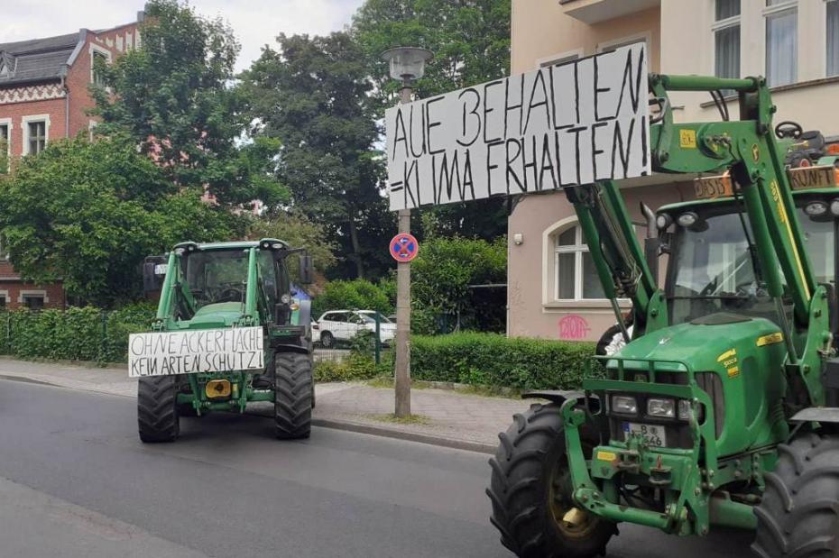 Auf einer Straße stehen zwei Traktoren mit Transparenten: Aue behalten = Klima erhalten. Und: Ohne Ackerfläche kein Artenschutz.