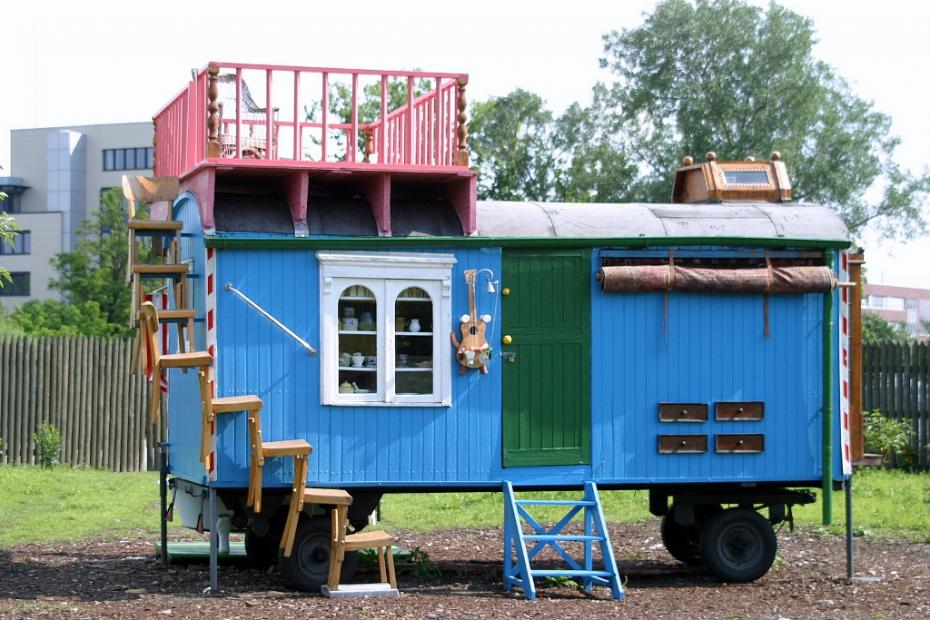 Blauer Bauwagen von Peter Lustig aus der Kinderserie Löwenzahn, eine Treppe aus Holzstühlen führt auf die pinkfarbene Dachterrasse.