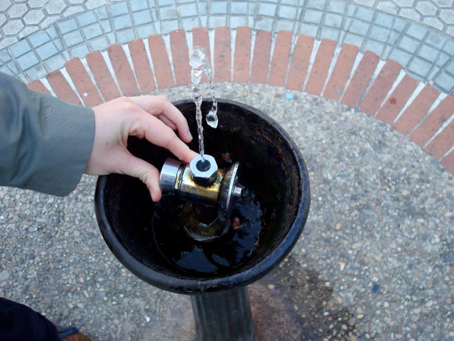 Jemand lässt aus einem öffentlichen Trinkwasserbrunnen Wasser hochsprudeln.