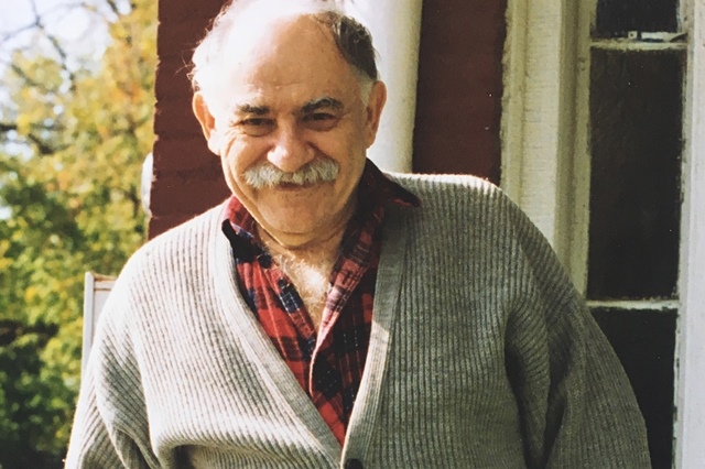Murray Bookchin, er eine Halbglatze, einen Schnurrbart und ein rot.schwarz karriertes Hemd und eine graue Jacke an hat.