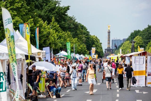Zu sehen ist die Straße des 17.Juni auf der das Umweltfestival stattfindet. Es gibt mehrer Stände und Menschen, die an den Ständen sind oder daran vorbeilaufen.