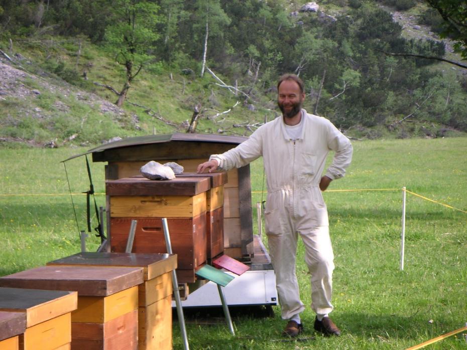 Ein Foto von Walter Haefeker, der neben Bienenstöcken in einen weißen Imkarnazug steht.